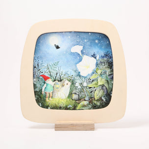 A toverlux frame with rounded corners, featuring a colorful fantasy illustration of a small gnome, a white rabbit, a large white flower, and a starry night sky, mounted on a light wood stand against a white background.