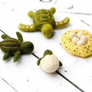 Felted turtle toys and a nest with eggs on a white wooden surface