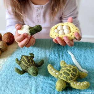 Child holding felt turtle and nest toys on a blue blanket