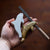 Hand holding Studiostone creative's unfinished soapstone Orca shape next to a completed one and a file | Conscious Craft 