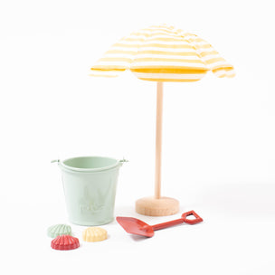 Maileg yellow and white stripe beach umbrella on wooden stand with beach bucket set including blue bucket, red spade and a set of three, red blue and yellow, shell sand moulds  | © Conscious Craft